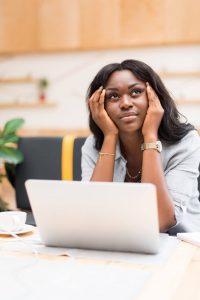 Black woman looking frustrated while sitting at laptop dealing with writer's block