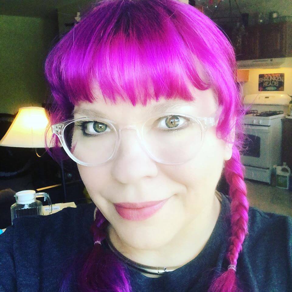 image of Ducky DooLittle wearing glasses, with pink hair, in dark shirt