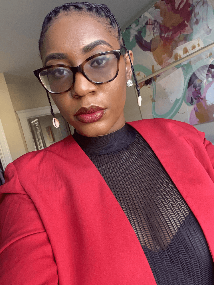bio image for Seshata Rose, wearing a red blazer and black mesh top underneath it -- Seshata is featured in our Smutlancer Spotlight for April 2021